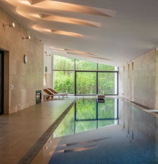 Deep swimming pool illuminated with lights in modern apartment with large windows in daytime
